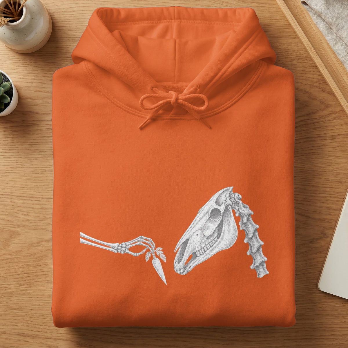Orange hoodie with skeletal hand offering carrot to horse skull graphic.