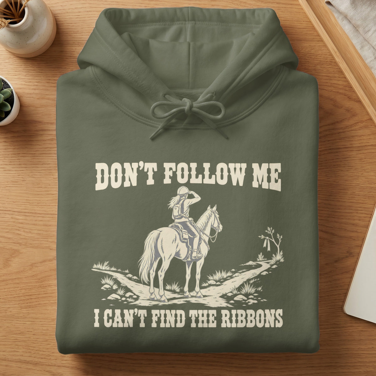 An olive green hoodie featuring a graphic of a horseback rider and the text DON'T FOLLOW ME I CAN'T FIND THE RIBBONS.