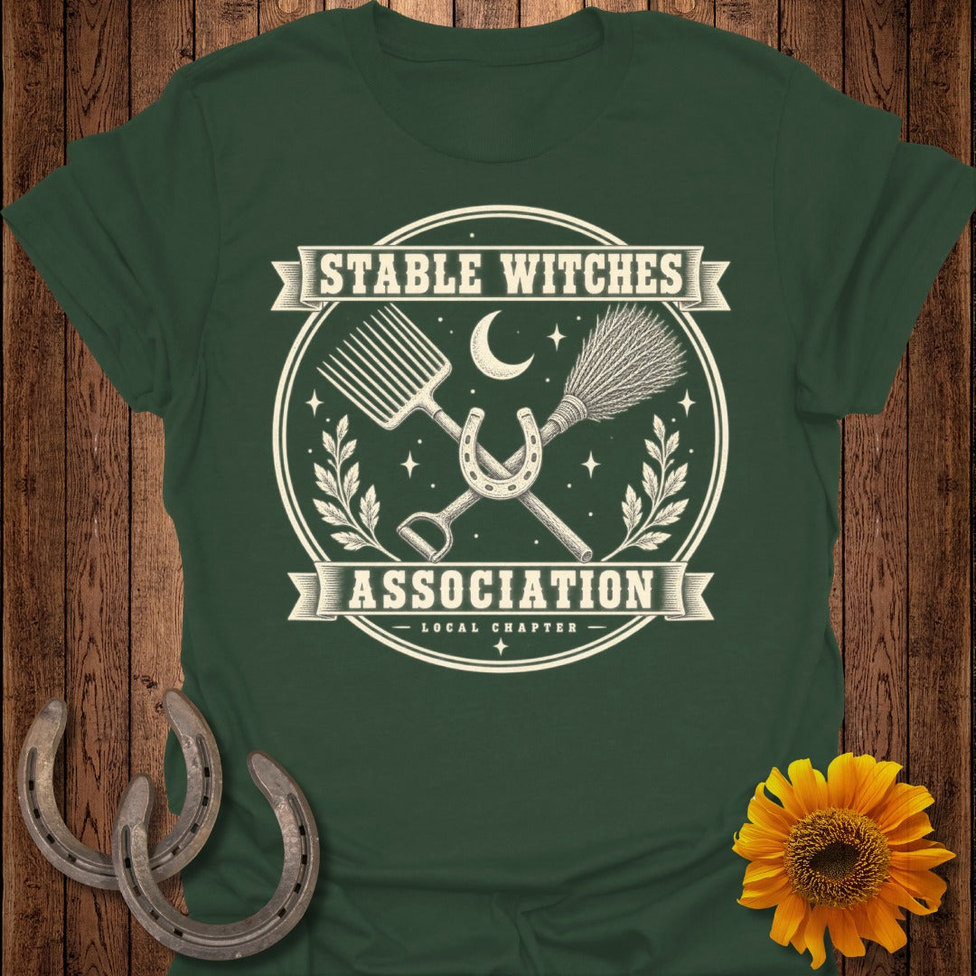 Green t-shirt with "Stable Witches Association" logo featuring pitchfork, broom, horseshoe, and moon.