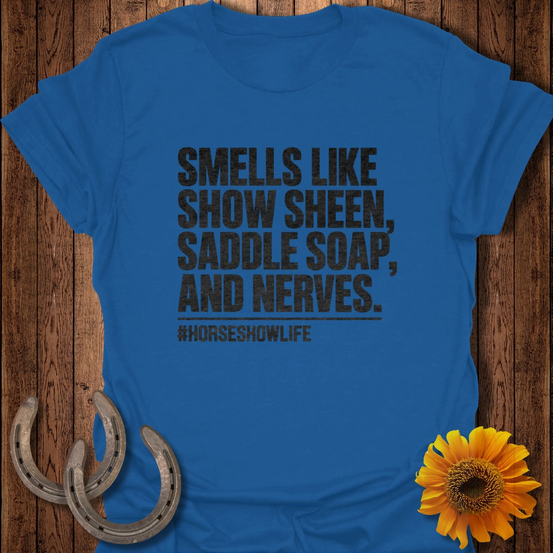 A blue t-shirt printed with the text SMELLS LIKE SHOW SHEEN, SADDLE SOAP, AND NERVES.