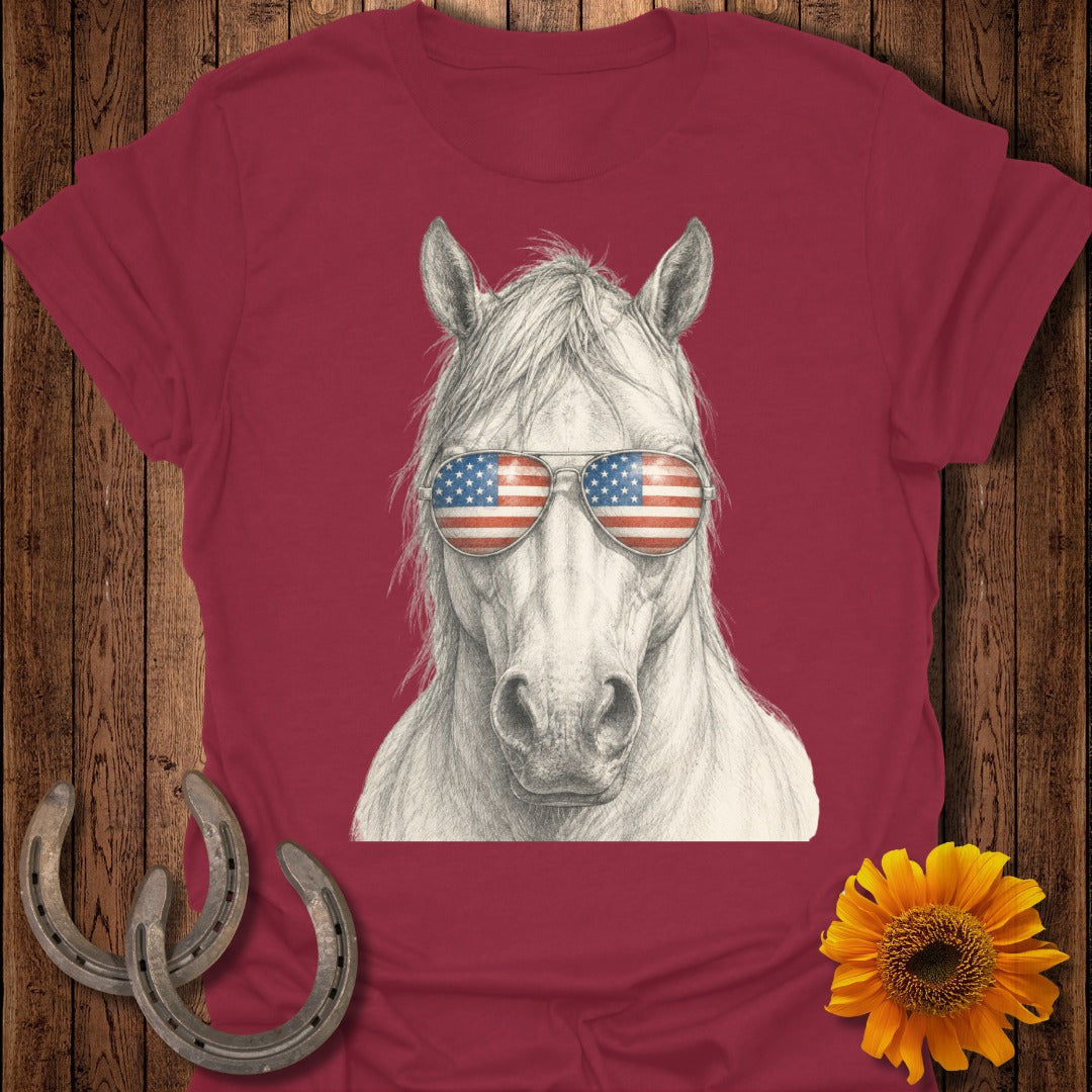 White horse wearing American flag sunglasses on a maroon t-shirt.