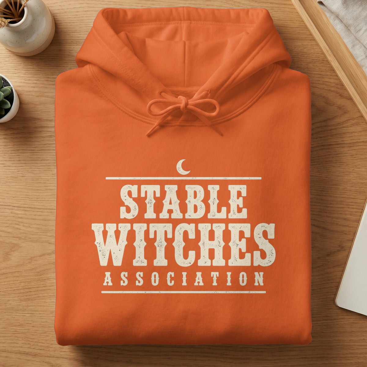 Orange hoodie with "Stable Witches Association" text and a crescent moon.