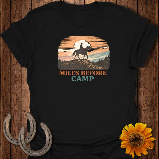 Black t-shirt graphic with cowboy on horse silhouetted against sunset, "Miles Before Camp" text.