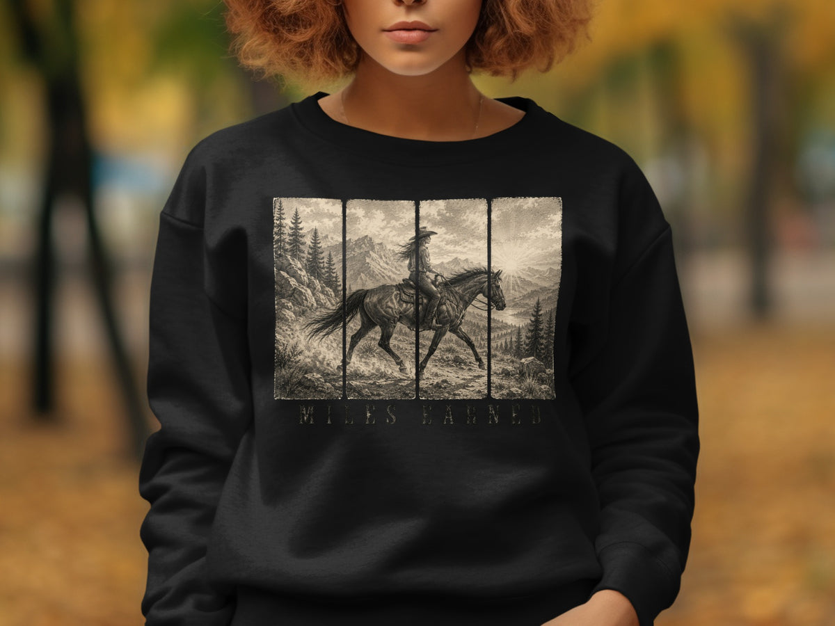 Black sweatshirt with vintage illustration of a rider on horseback in a mountain landscape and text.