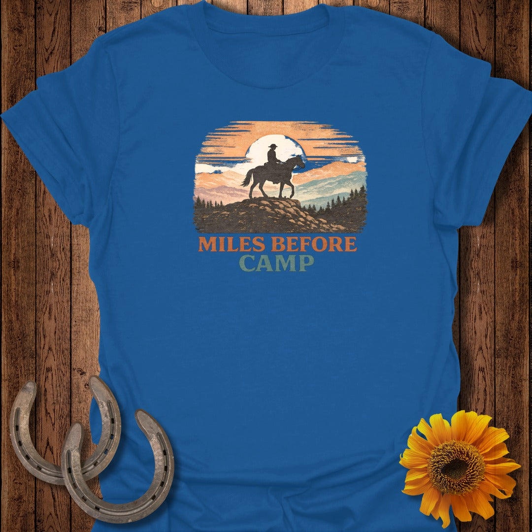 Blue t-shirt with graphic of a horse rider against a sunset and text "MILES BEFORE CAMP."