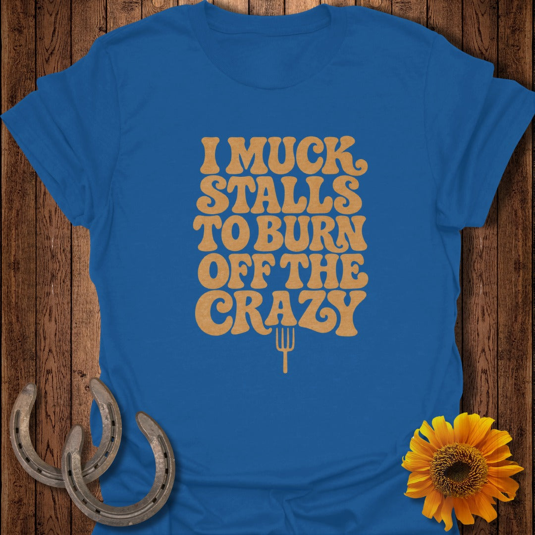 A blue T-shirt with the gold text I MUCK STALLS TO BURN OFF THE CRAZY.