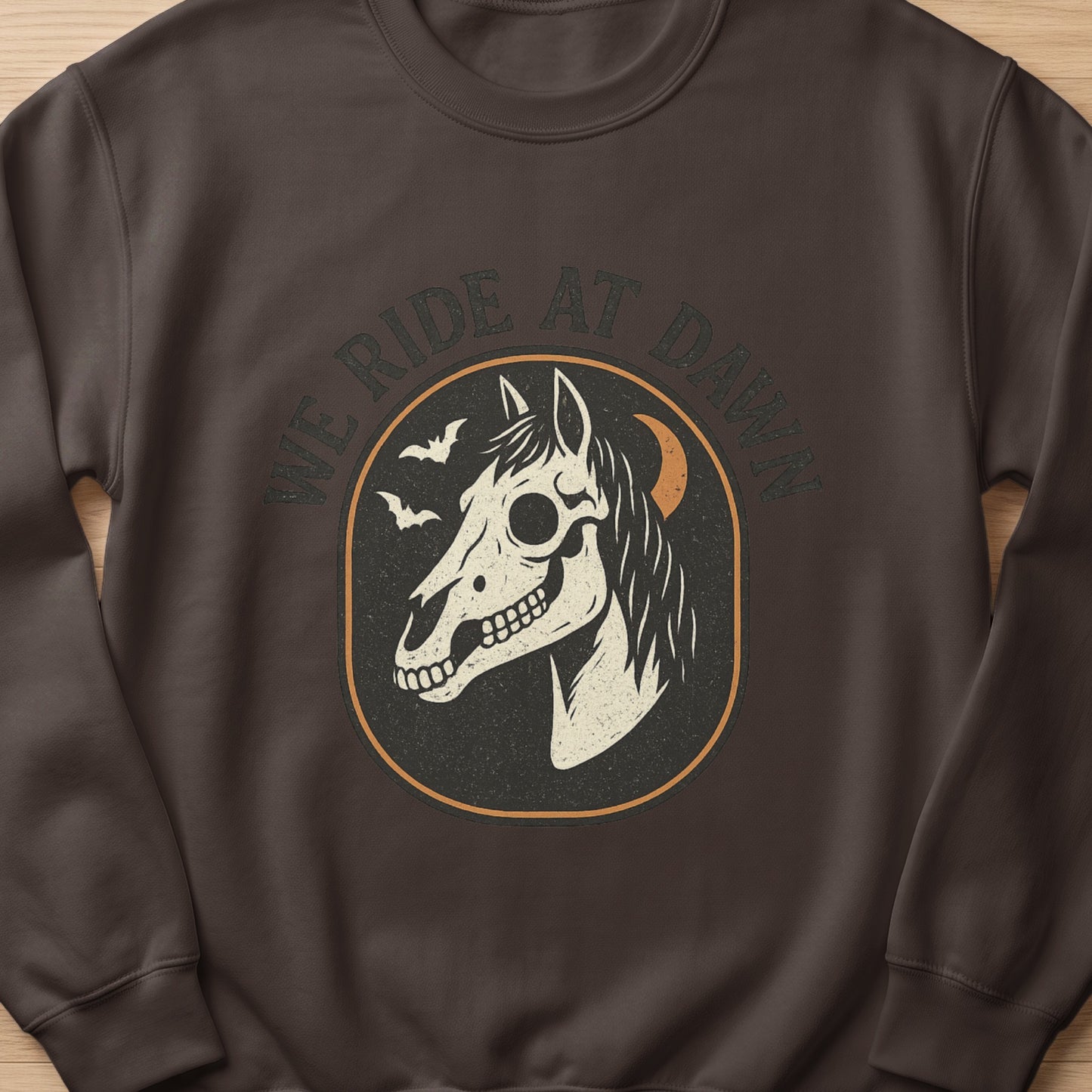 Brown sweatshirt with a graphic of a horse skull, bats, moon, and "WE RIDE AT DAWN" text.