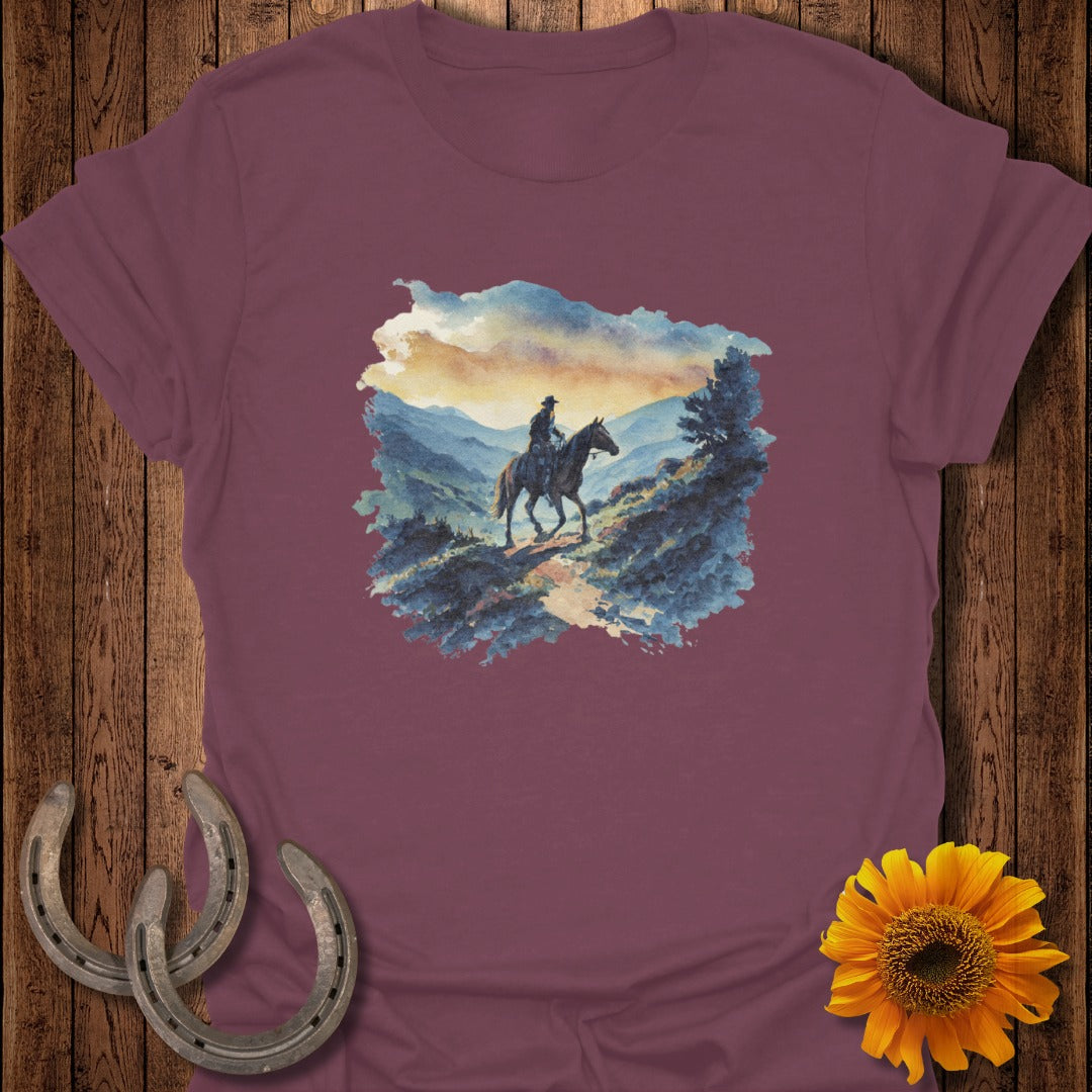 Cowboy on horseback in mountain landscape, watercolor painting graphic on maroon t-shirt.