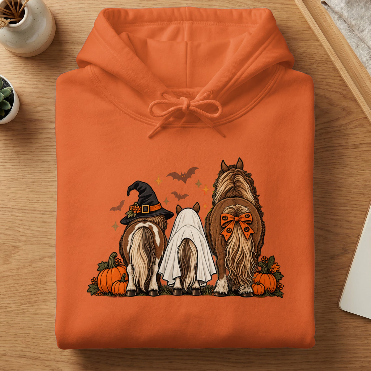 Orange hoodie with three horses wearing Halloween costumes: witch hat, ghost, and bow.