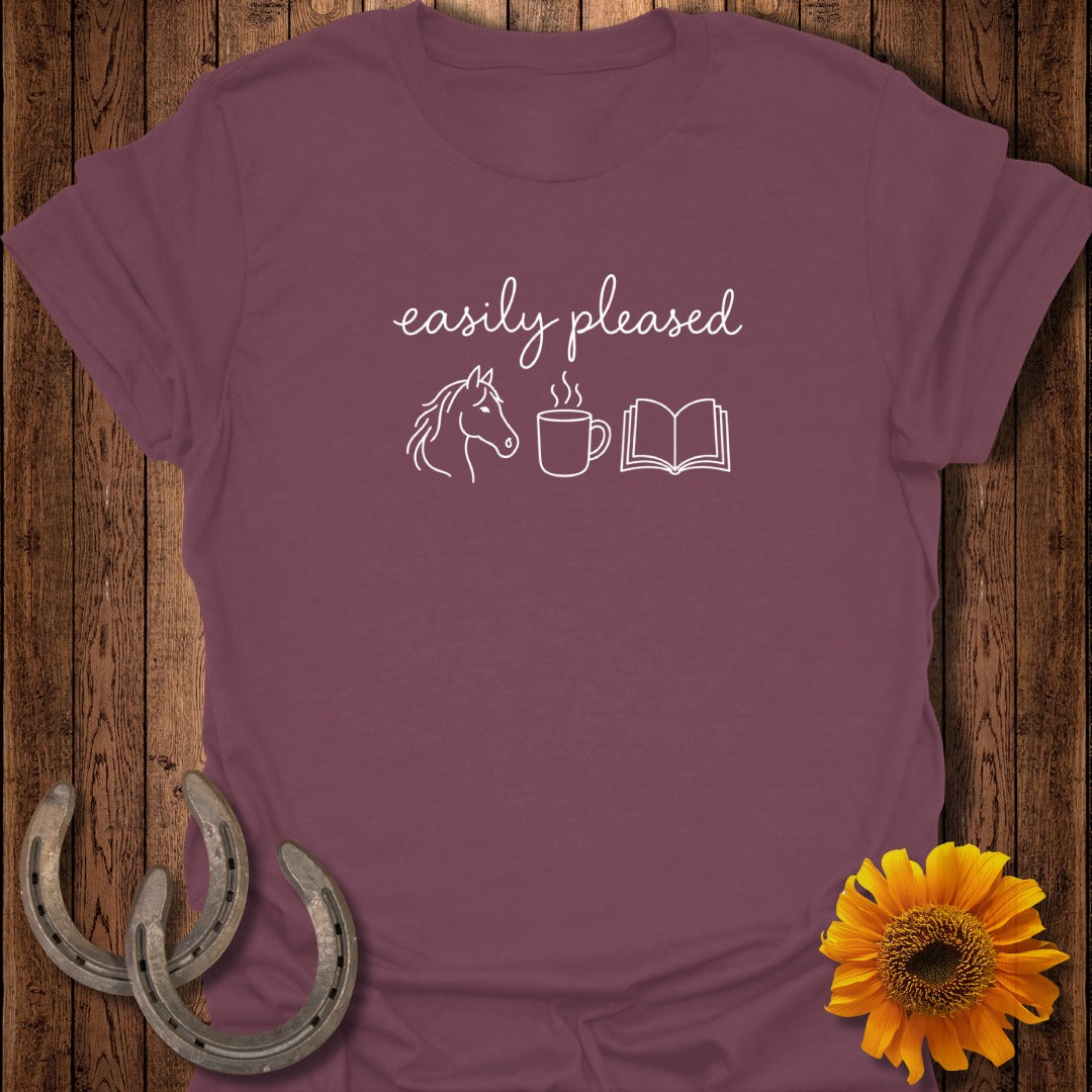 Maroon t-shirt featuring the text "easily pleased" and white outline icons of a horse, steaming coffee cup, and open book.