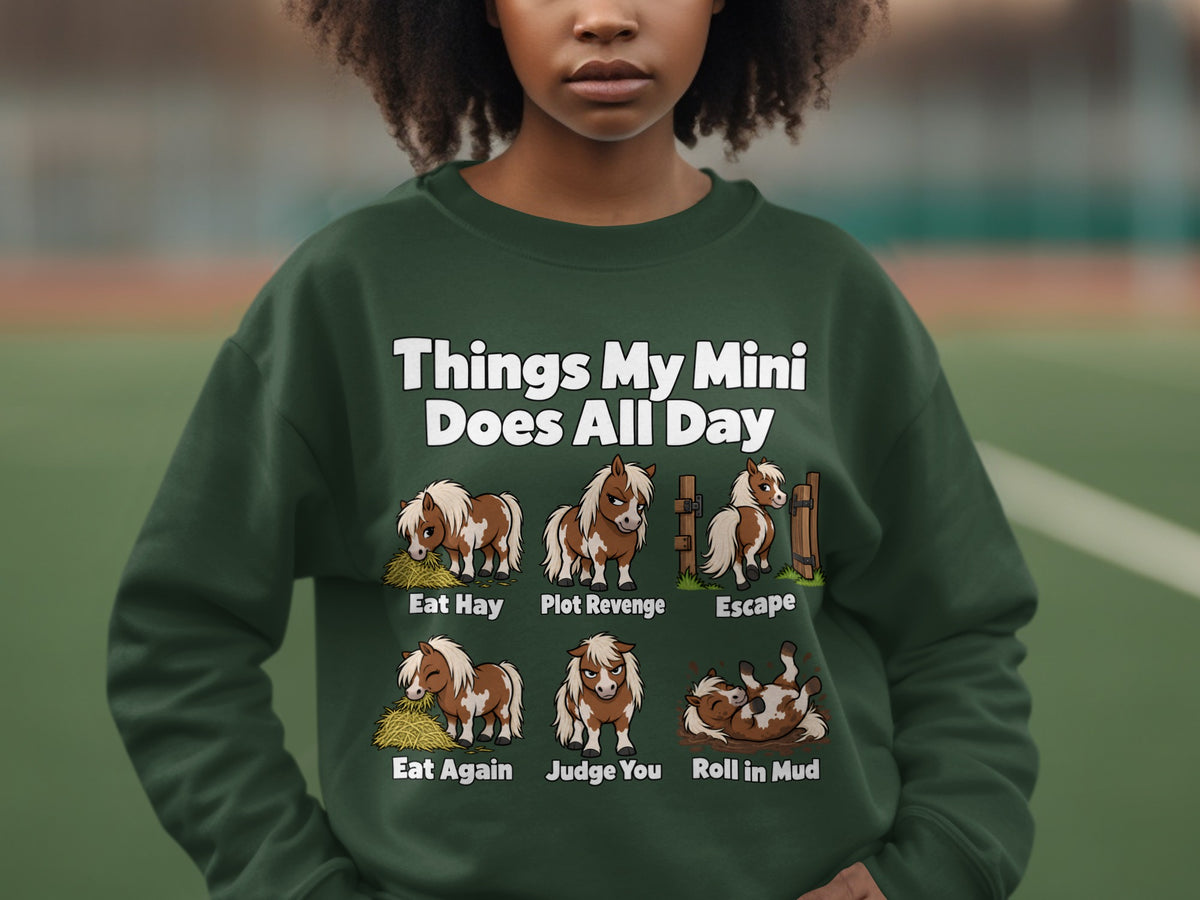 A person wearing a dark green sweatshirt printed with cartoon ponies and humorous text.