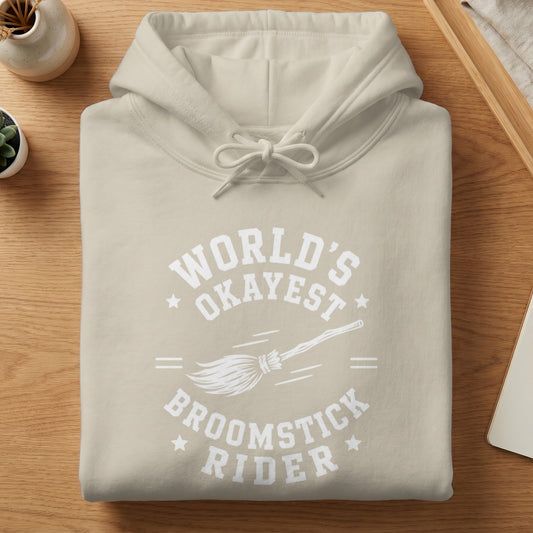 Beige hoodie with white "World's Okayest Broomstick Rider" text and broom graphic.