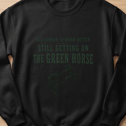 Black sweatshirt with green text "Old enough to know better still getting on the green horse" and horse graphic.