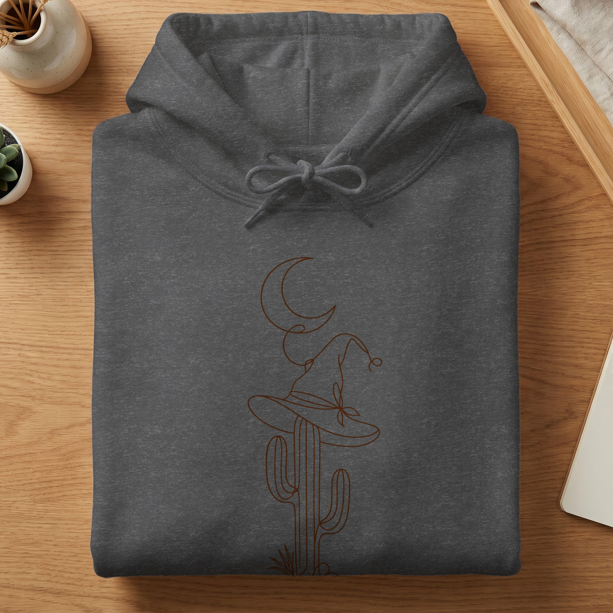 Dark grey hoodie with a brown line art of a cactus, moon, and witch hat.