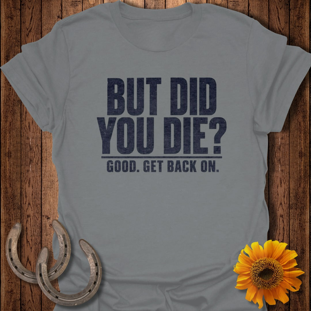 A gray short-sleeve t-shirt with black text that reads "BUT DID YOU DIE? GOOD. GET BACK ON." displayed on a wooden background with horseshoes and a sunflower.