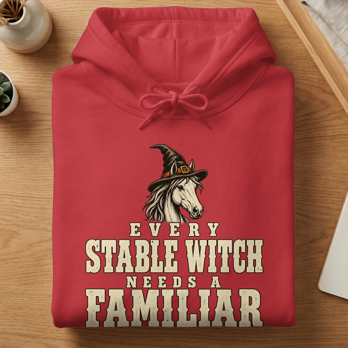 Red hoodie with horse wearing witch hat and text "Every Stable Witch Needs a Familiar".