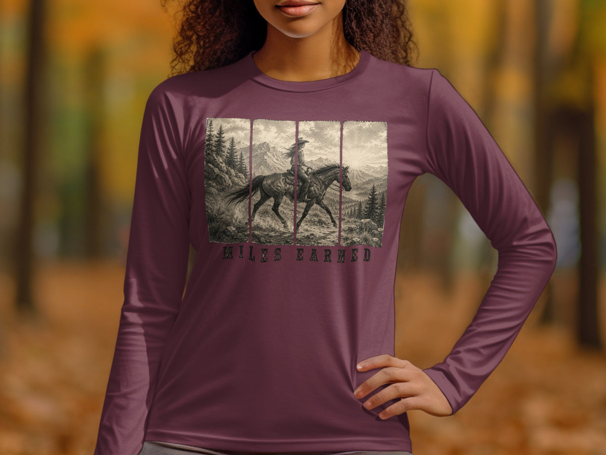 Long-sleeve shirt with a vintage-style print of a woman on horseback in a mountain landscape, text "MILES EARNED".