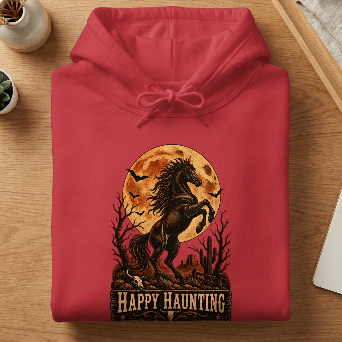 Red hoodie with a Halloween-themed desert graphic featuring a horse, moon, bats, and "Happy Haunting" text.