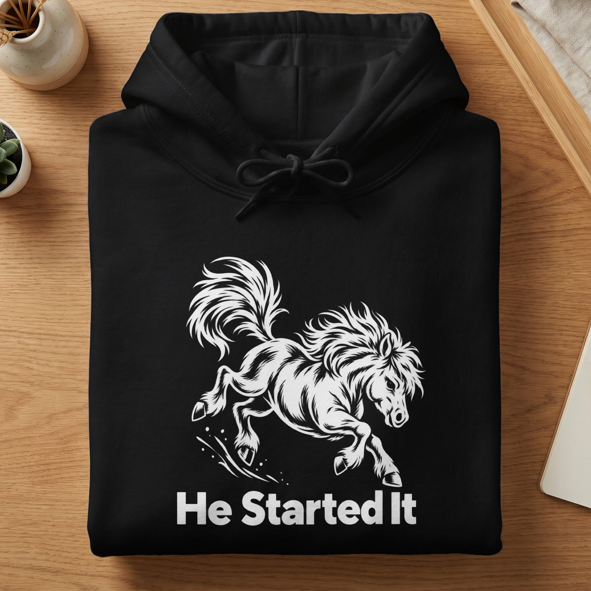 Folded black hoodie with white graphic of a galloping horse and text He Started It.