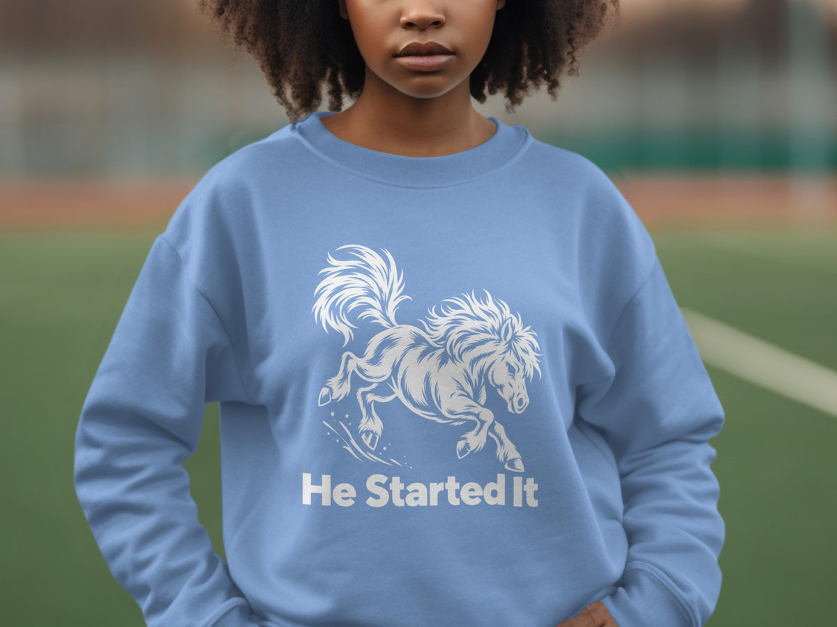 A person wearing a blue sweatshirt with a white graphic of a running horse and the text He Started It.