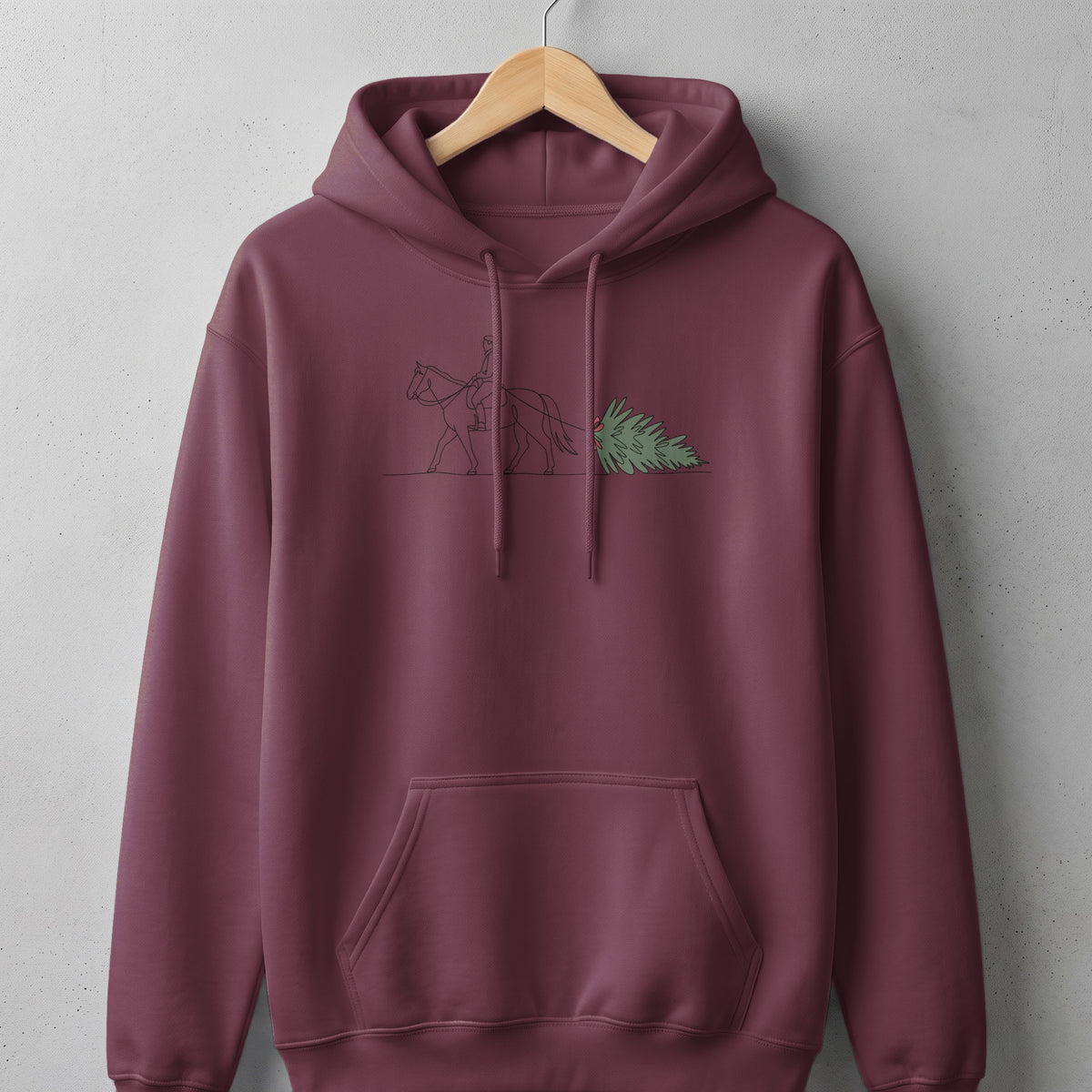 Burgundy hoodie with a line drawing of a person riding a horse pulling a Christmas tree.