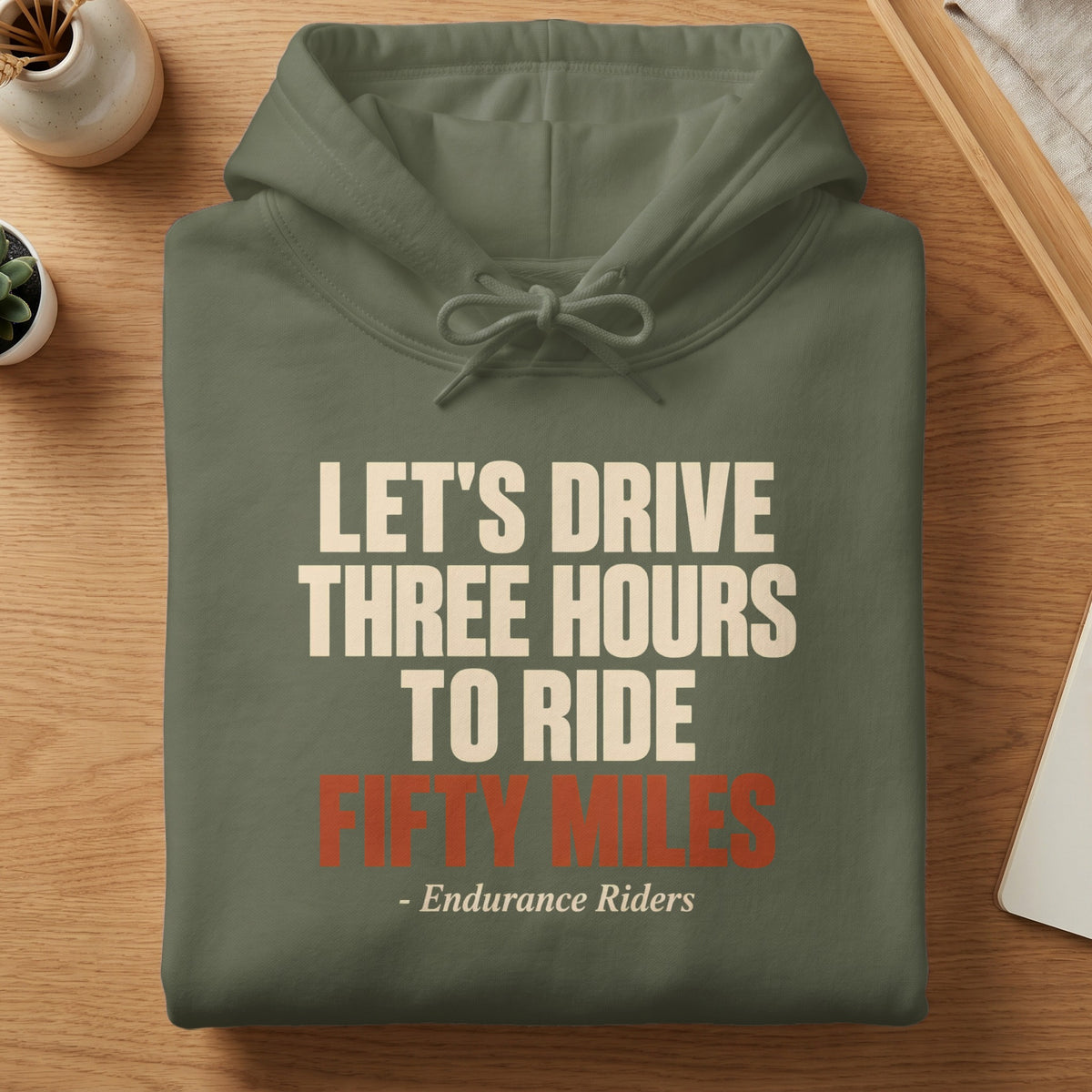 Folded green hoodie with the text LET'S DRIVE THREE HOURS TO RIDE FIFTY MILES - Endurance Riders.
