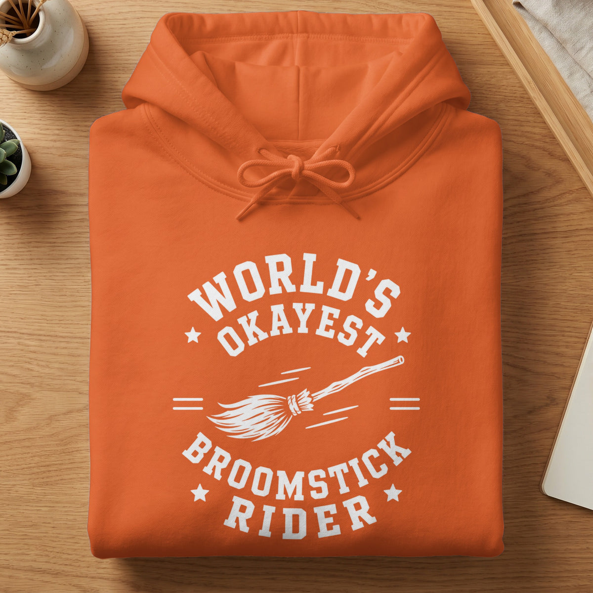 Orange hoodie with white text: "World's Okayest Broomstick Rider" and broom graphic.