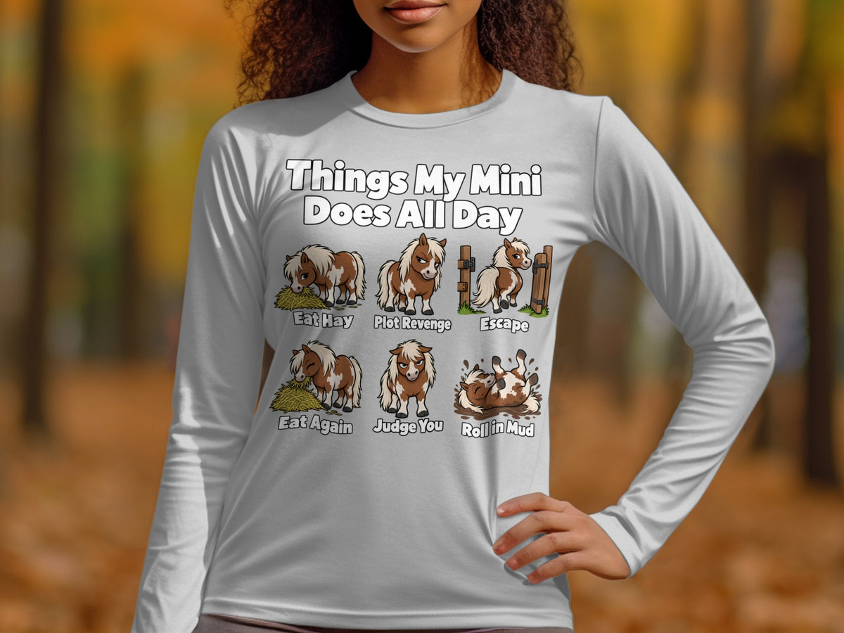 A person wearing a light gray long-sleeve shirt with a graphic about miniature horse daily activities.
