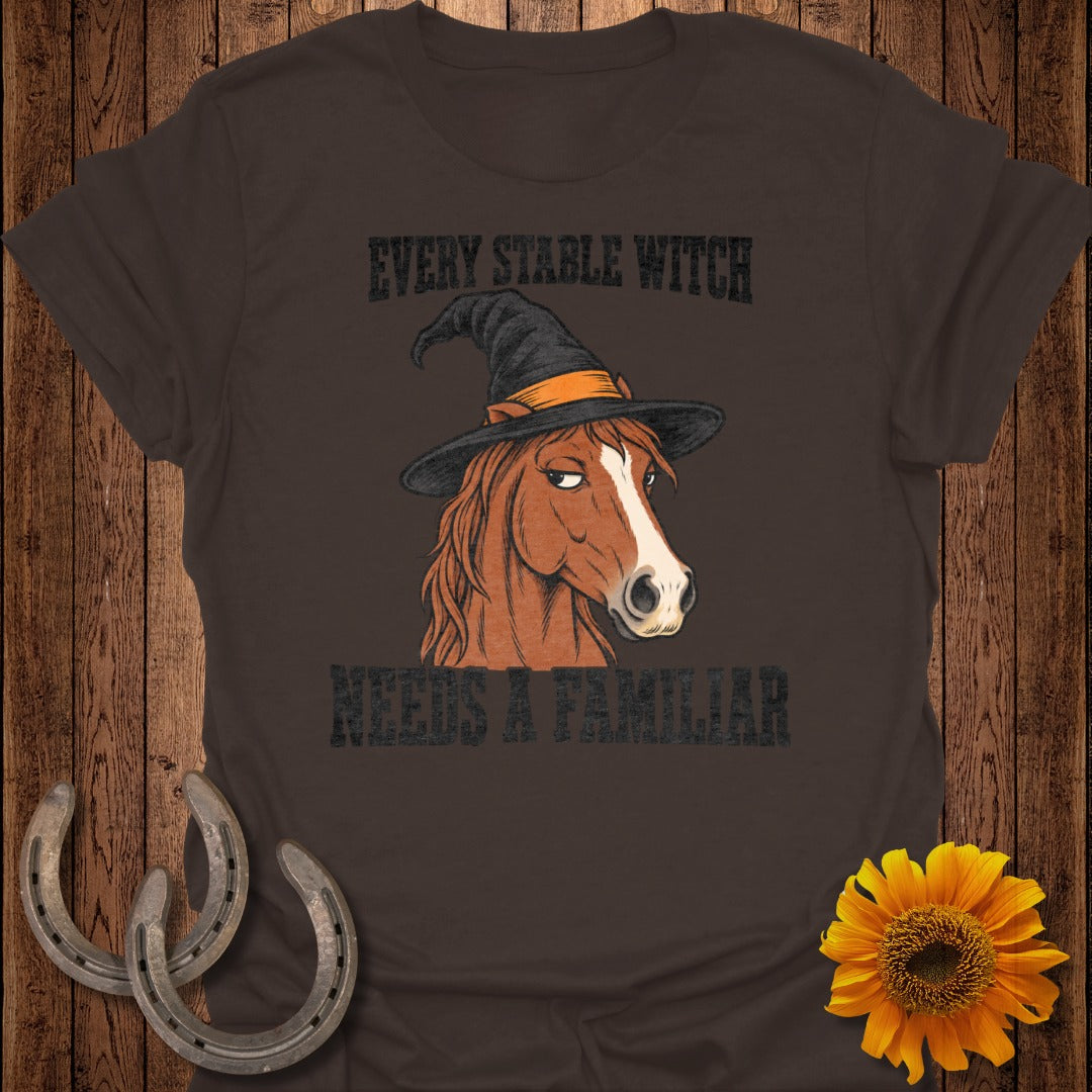 Brown t-shirt with a horse wearing a witch hat and the text "Every Stable Witch Needs a Familiar."
