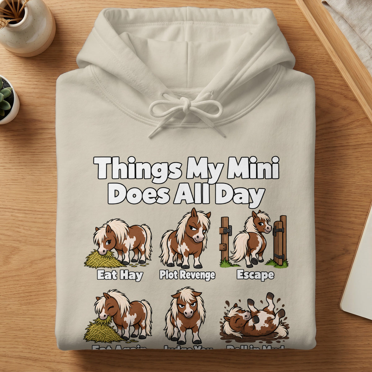 A cream-colored hoodie features a graphic of a brown and white miniature horse doing various activities with humorous text labels.