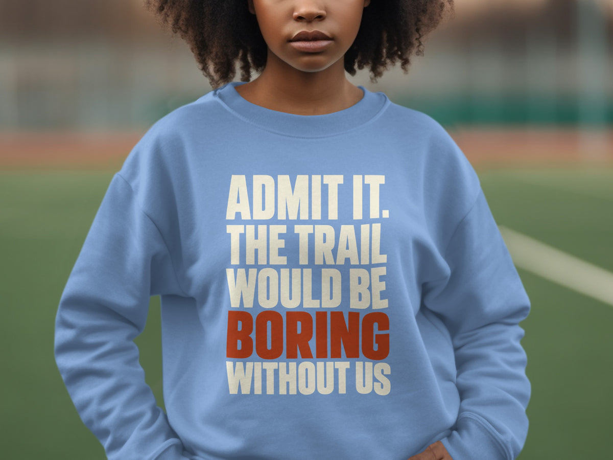 A person wearing a light blue crewneck sweatshirt with the text Admit It. The Trail Would Be Boring Without Us printed on the chest.