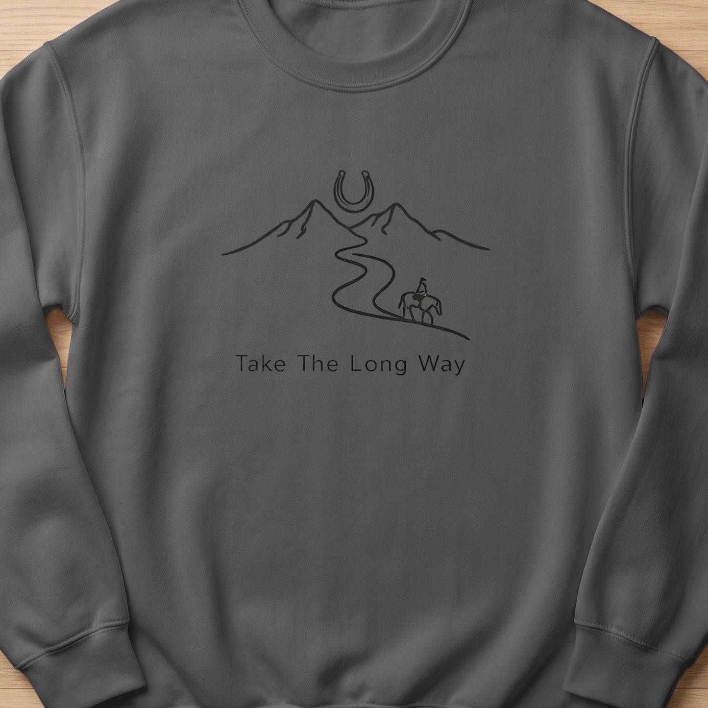 Dark grey sweatshirt with a line drawing of a horseshoe over mountains and a rider on a path, text "Take The Long Way".