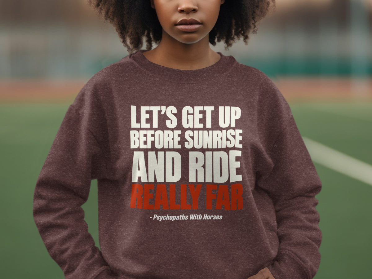 A person wearing a brown sweatshirt with white and red text reading Let's Get Up Before Sunrise And Ride Really Far.
