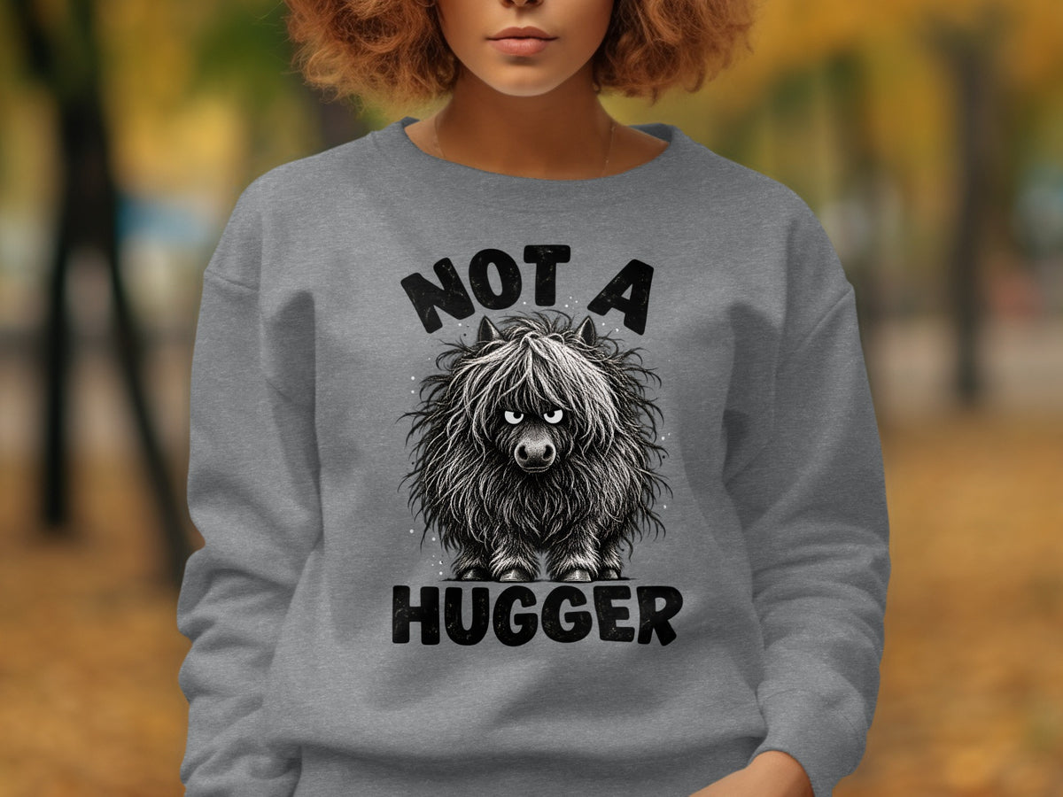 Grey sweatshirt with "NOT A HUGGER" text and a fluffy, black Highland cow graphic.