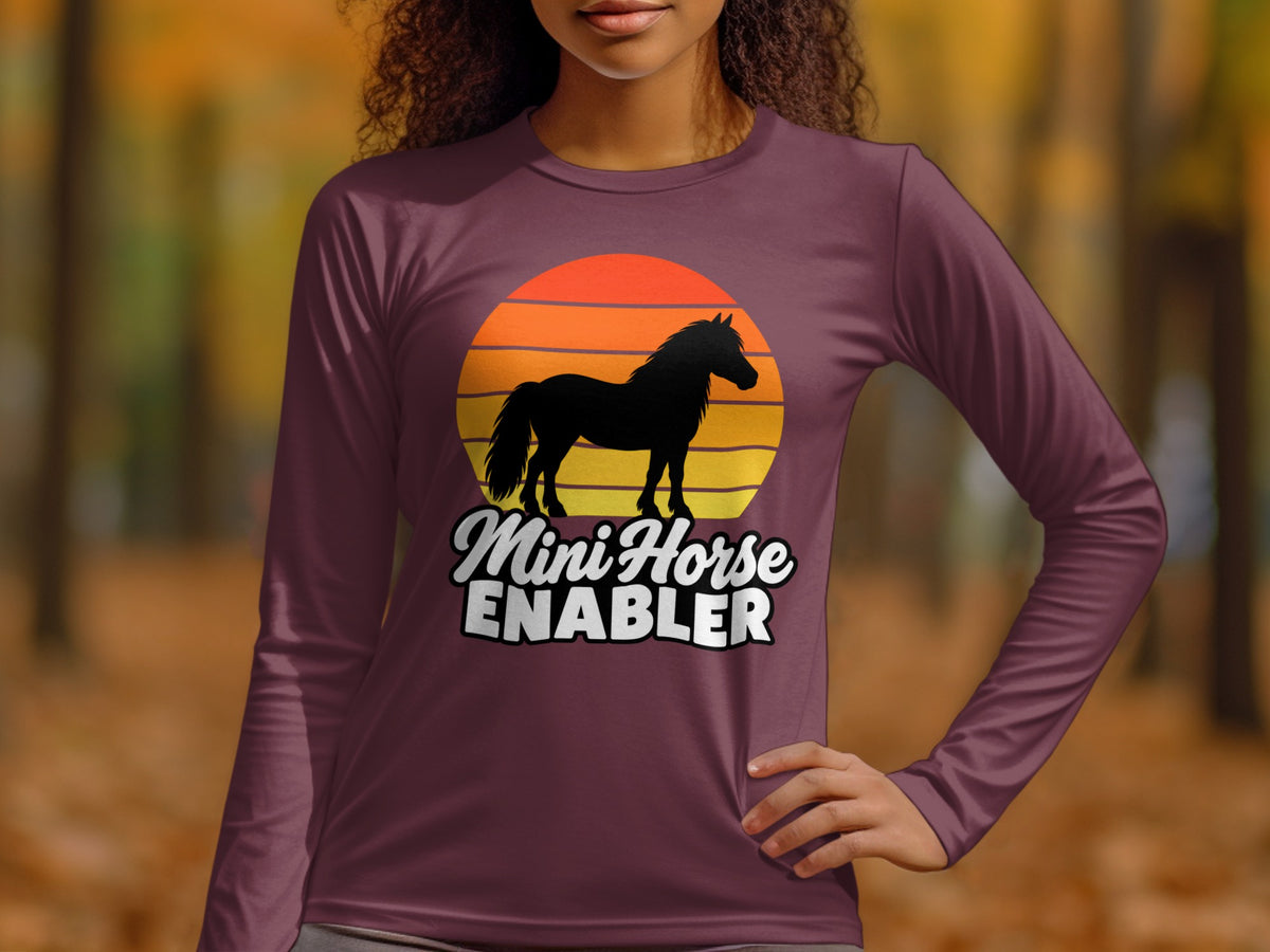 A person wearing a maroon long-sleeve shirt featuring a horse silhouette over a sunset and the text "Mini Horse Enabler".