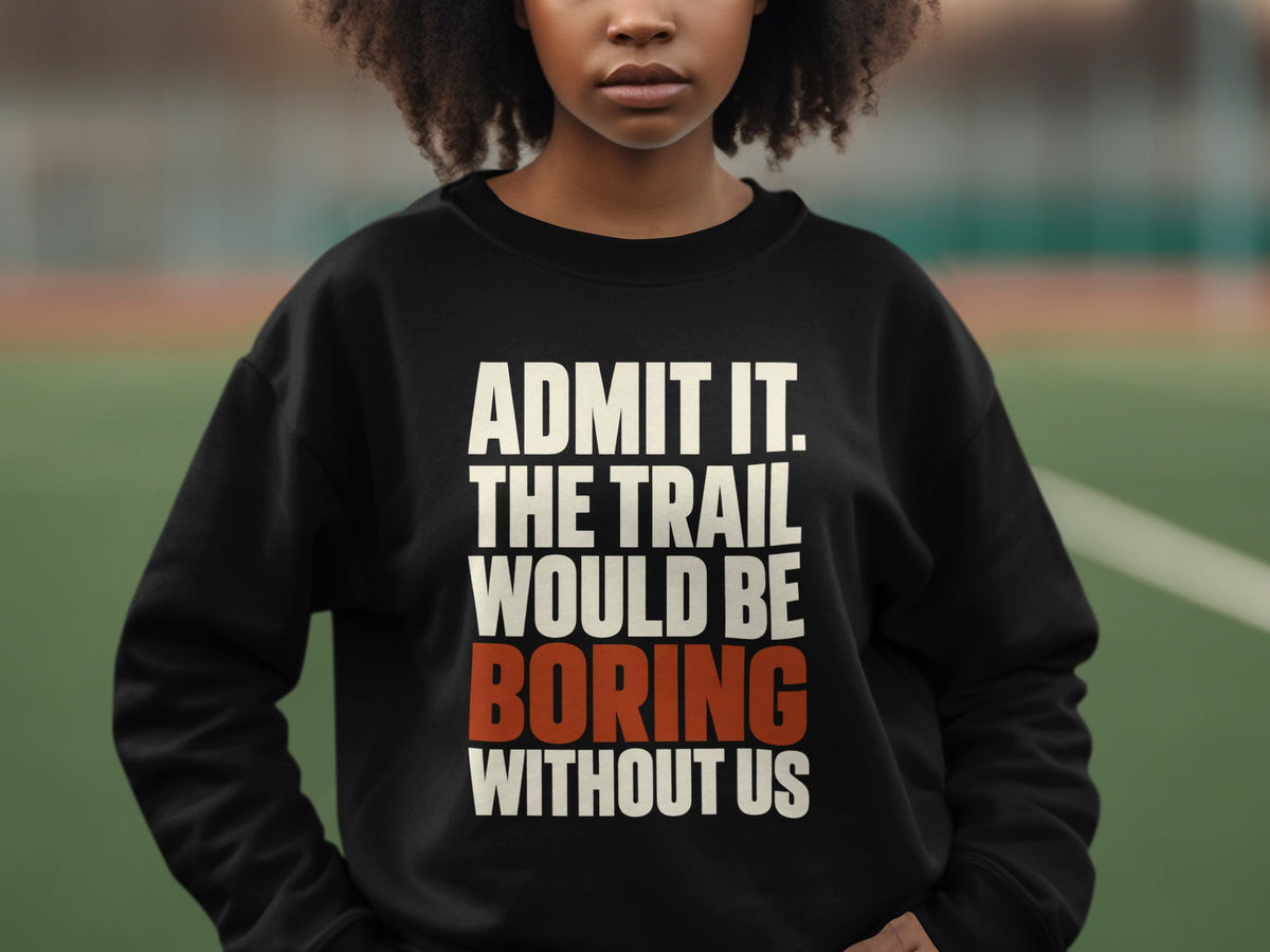 A person with curly hair wears a black crewneck sweatshirt featuring the text ADMIT IT. THE TRAIL WOULD BE BORING WITHOUT US.