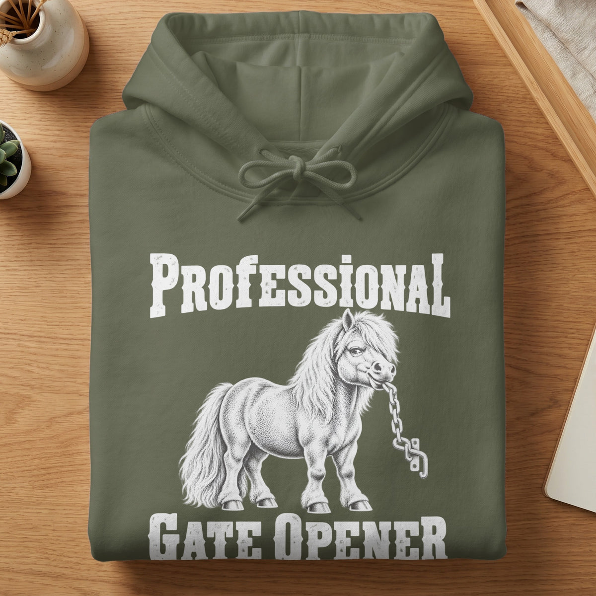 Folded olive green hoodie with white graphic text reading Professional Gate Opener and a sketch of a pony holding a chain.