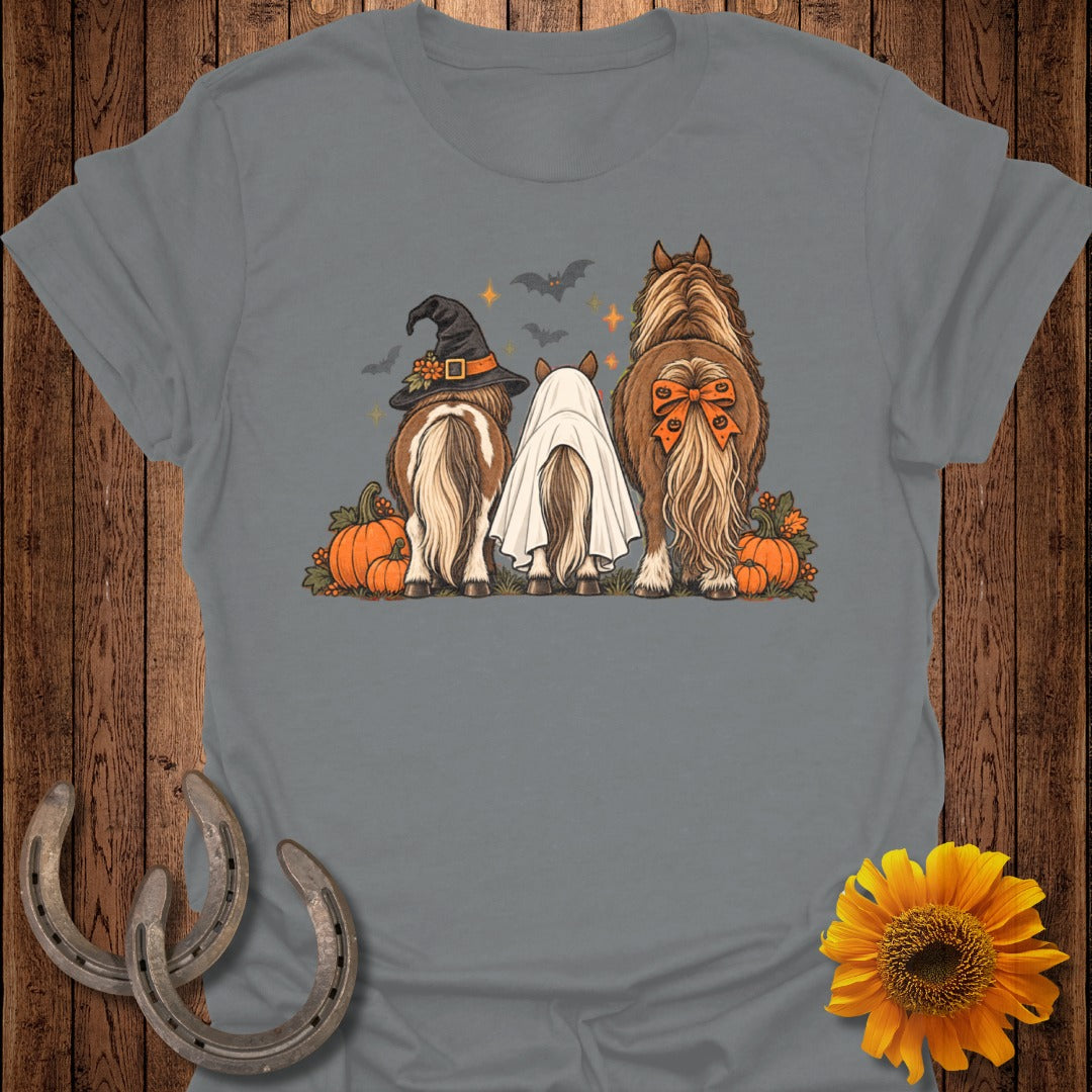 Three horses, one in a witch hat, one as a ghost, and one with a bow, with pumpkins.