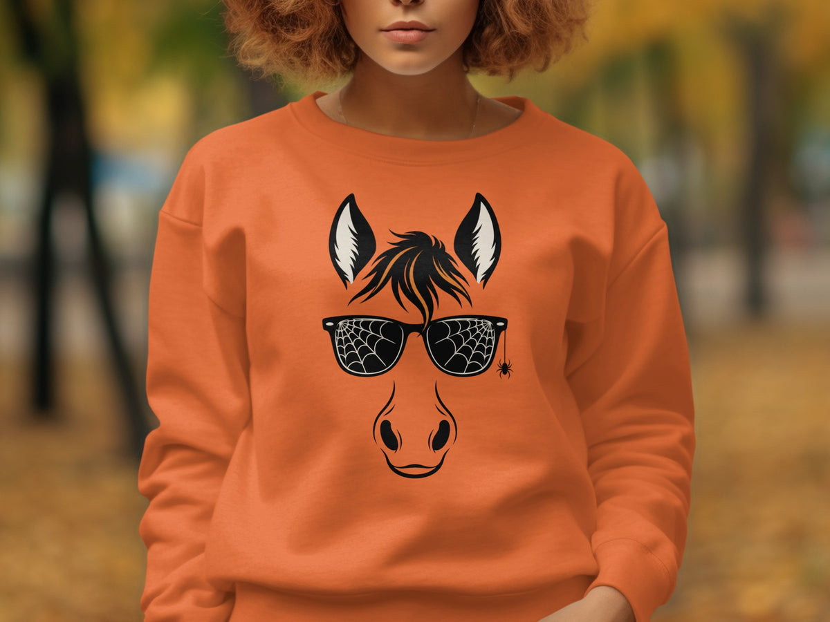 Horse wearing spiderweb sunglasses with hanging spider graphic on orange sweatshirt.