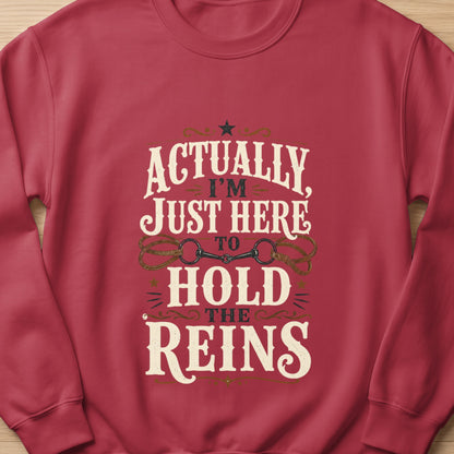 Red sweatshirt with "Actually, I'm Just Here To Hold The Reins" text and horse bit graphic.