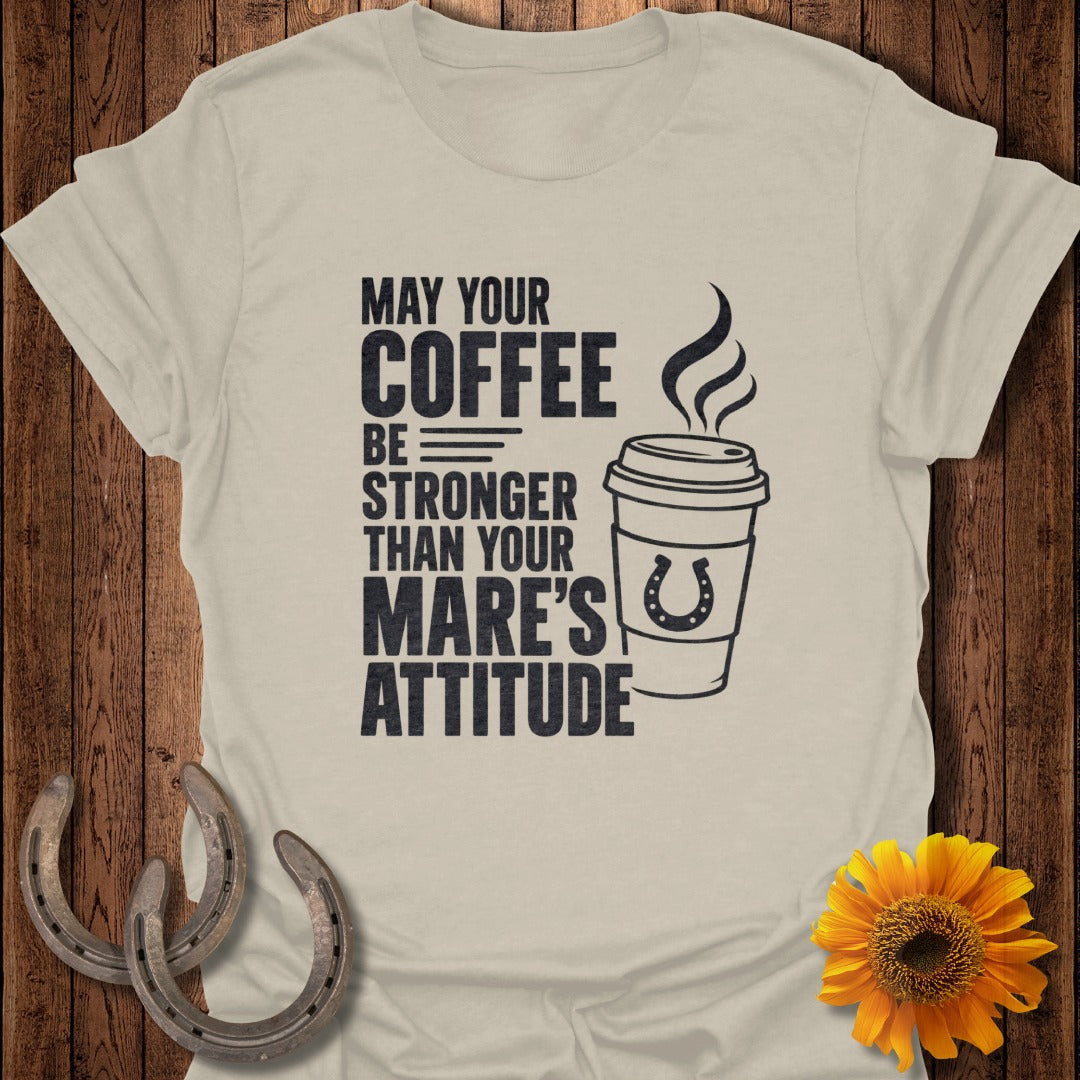 A beige t-shirt with black text that reads May your coffee be stronger than your mare’s attitude next to a coffee cup graphic with a horseshoe.