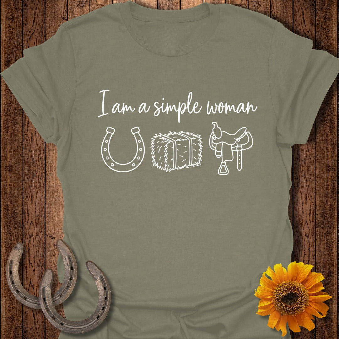 An olive green t-shirt with white text reading "I am a simple woman" and icons of a horseshoe, hay bale, and saddle.