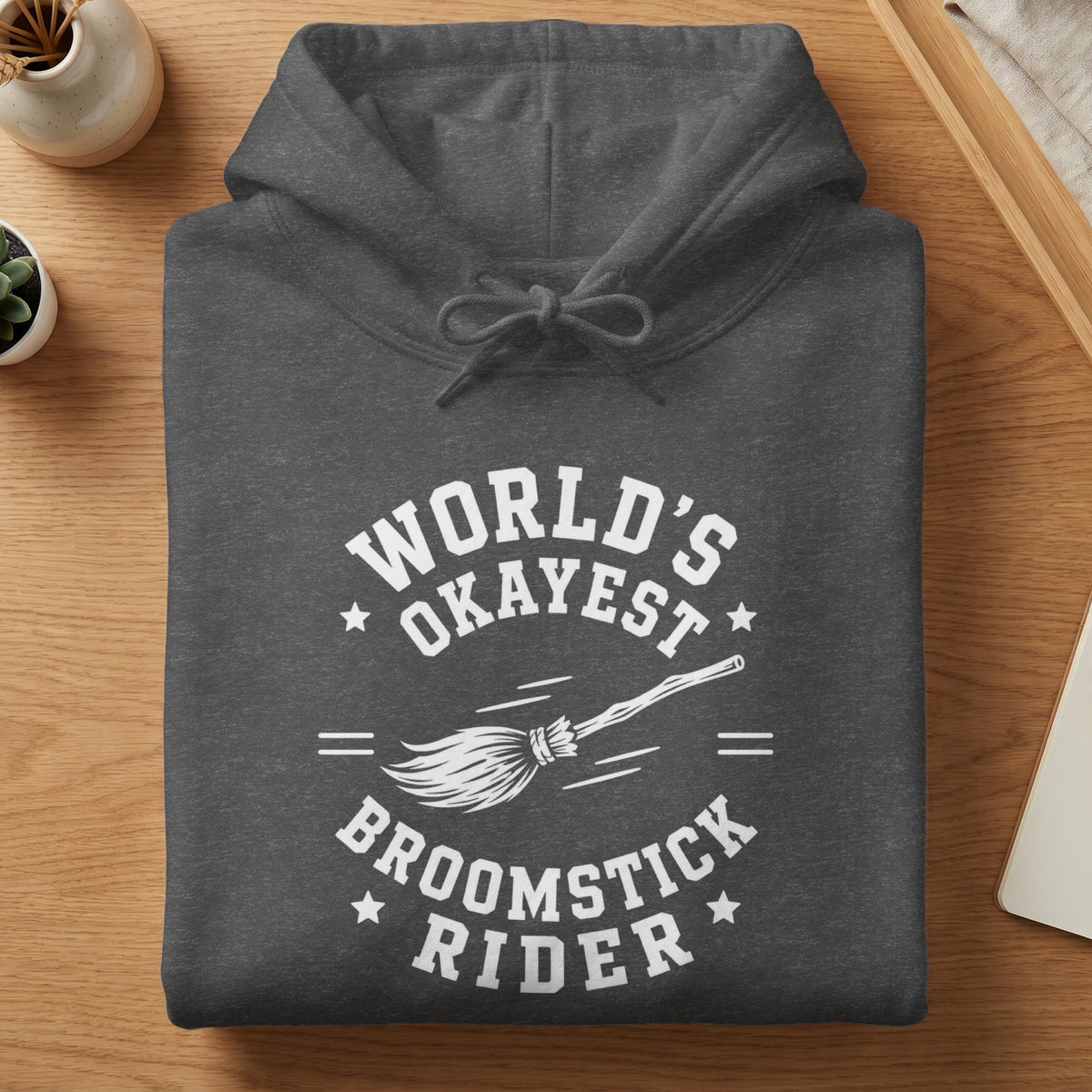 Dark grey hoodie with "World's Okayest Broomstick Rider" text and broom graphic.
