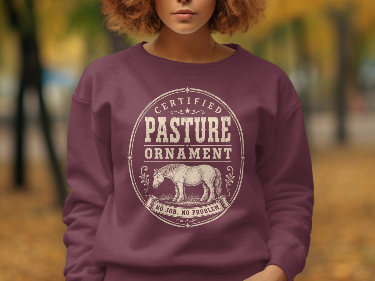 Maroon sweatshirt with a circular graphic featuring a horse and text: "CERTIFIED PASTURE ORNAMENT NO JOB. NO PROBLEM."