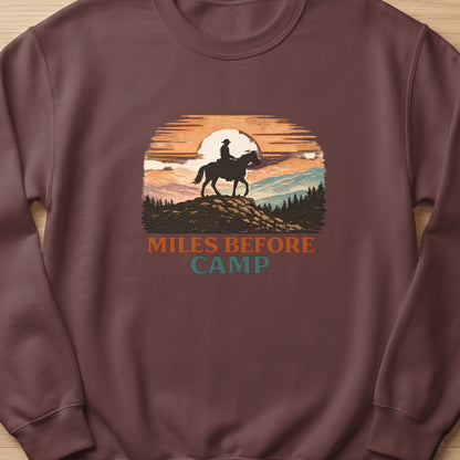Crewneck sweatshirt with a sunset graphic of a cowboy on horseback with text "MILES BEFORE CAMP".