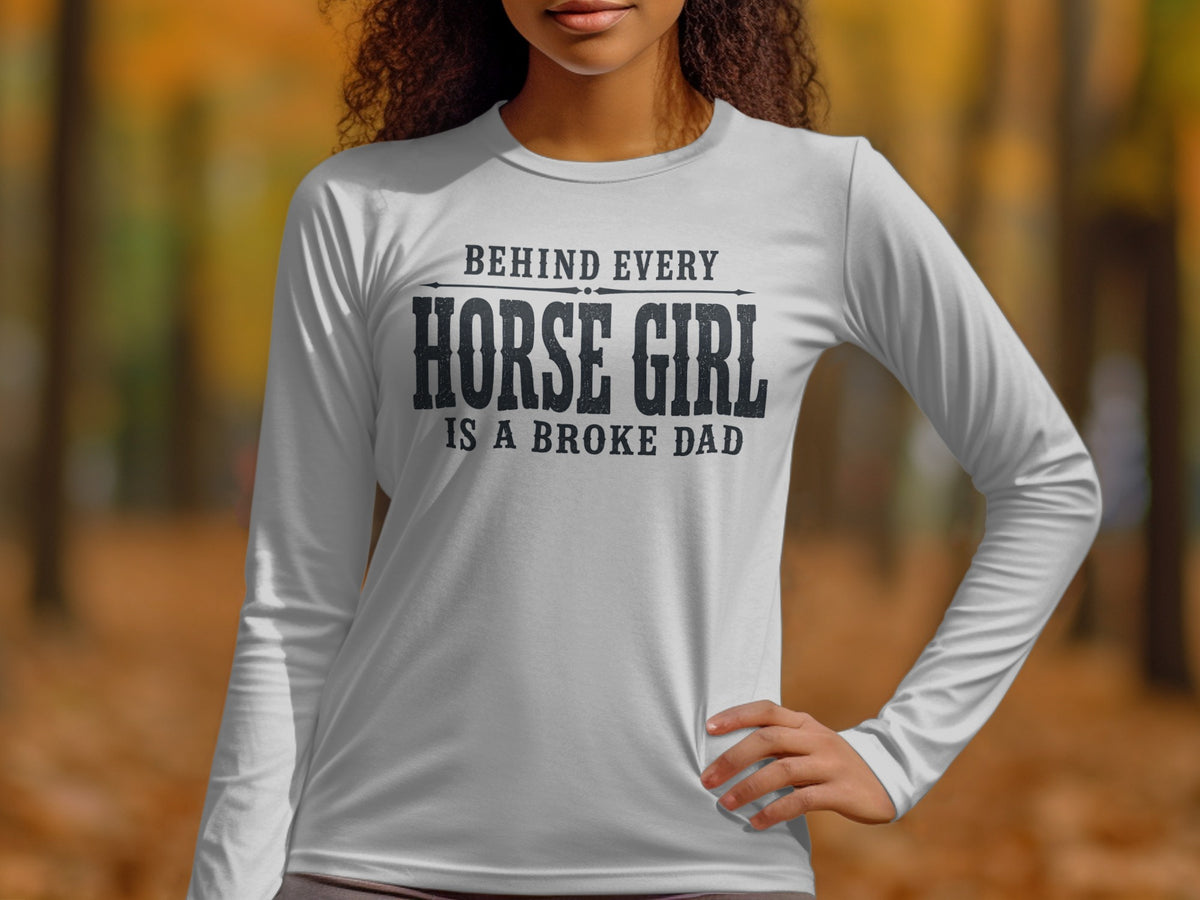 White long-sleeve shirt with black text: "Behind every horse girl is a broke dad".