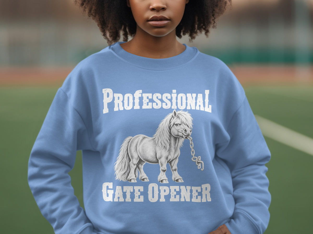 A person wearing a light blue crewneck sweatshirt featuring a graphic of a pony holding a chain in its mouth, with the text Professional Gate Opener above and below the pony.