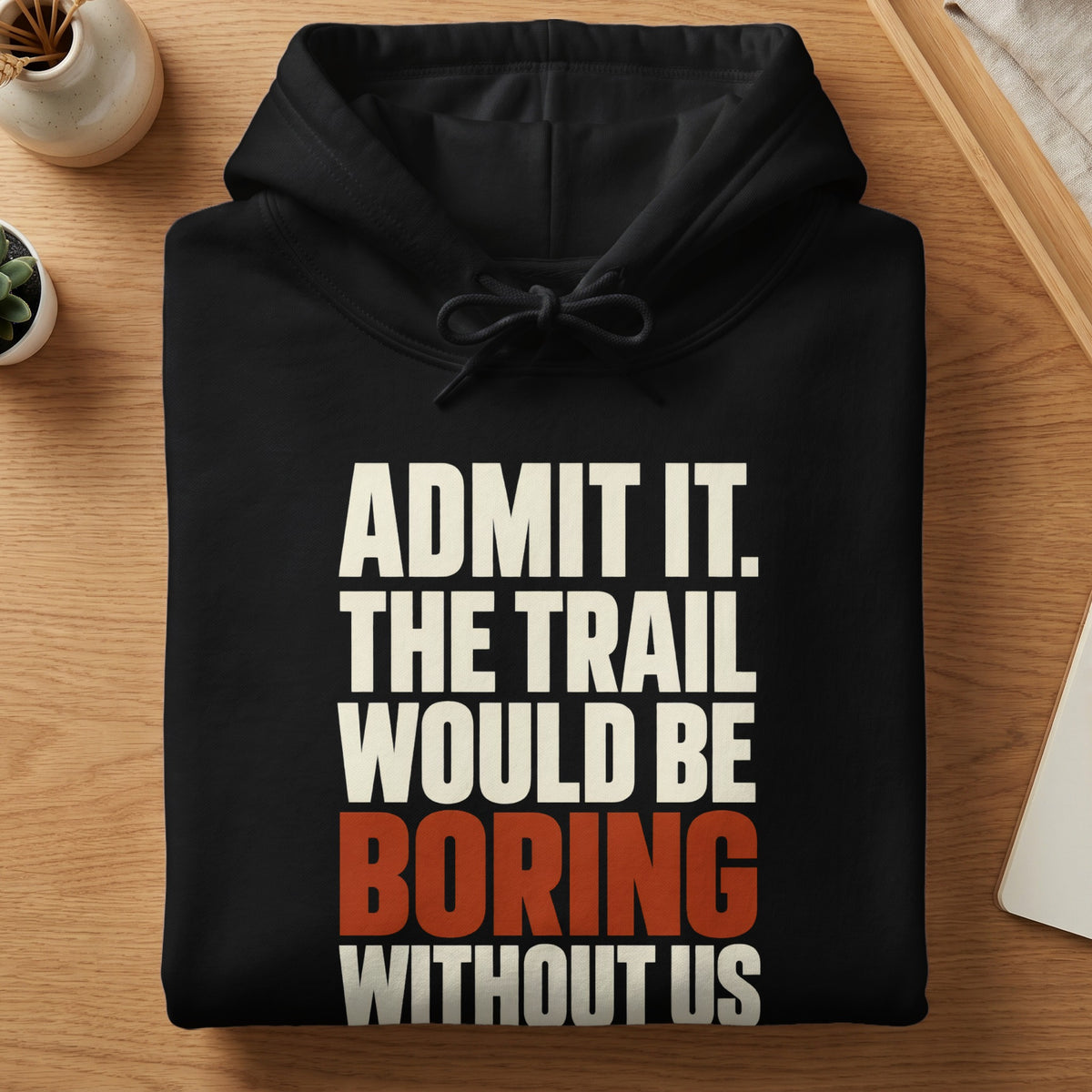 A folded black hoodie features the white and orange text "ADMIT IT. THE TRAIL WOULD BE BORING WITHOUT US."