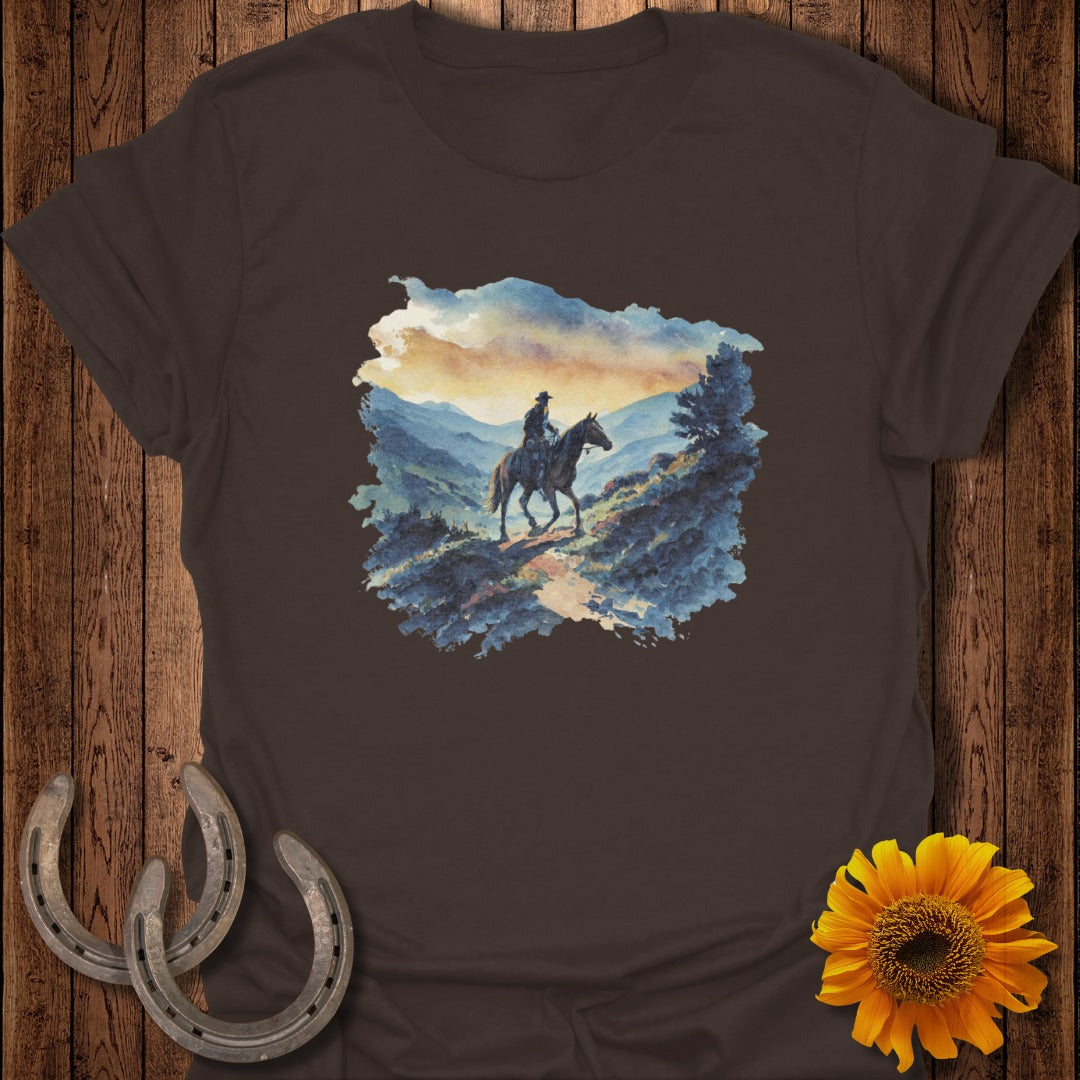 Brown t-shirt featuring a watercolor painting of a cowboy on horseback in a mountainous landscape.