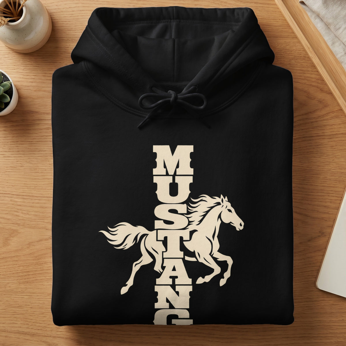 A folded black hoodie features a cream-colored graphic of a running horse and vertical Mustang text.